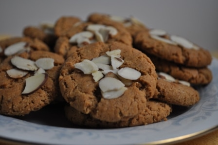 Plate full of crispy golden almond butter cookies with sliced almonds on top.