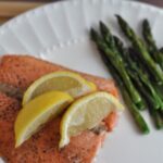 Baked Fresh Salmon at 350 in oven on a plate topped with 3 lemons next to fresh cooked asparagus