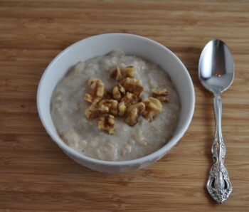 White Bowl with healthy banana oatmeal topped with walnuts. Spoon on right side of bowl.