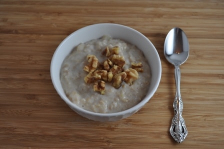 White Bowl with healthy banana oatmeal topped with walnuts. Spoon on right side of bowl.