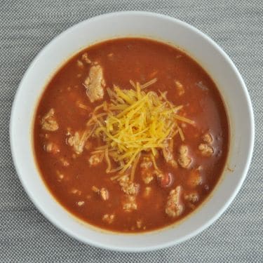 Chili topped with shredded cheddar cheese in a white bowl.