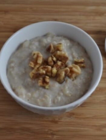 Banana oatmeal in a white bowl with spoon to the right side. Topped with walnuts.
