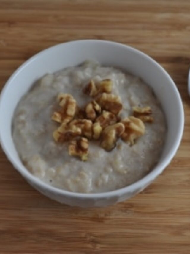 Banana oatmeal in a white bowl with spoon to the right side. Topped with walnuts.