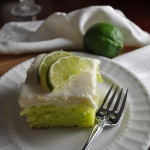 Piece of Key Lime Cake Topped with Fresh Lime Mint Green Color on White Plate with Linen Napkins