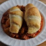 Italian casserole with crescent rolls and ground chicken in tomato sauce on a white plate.