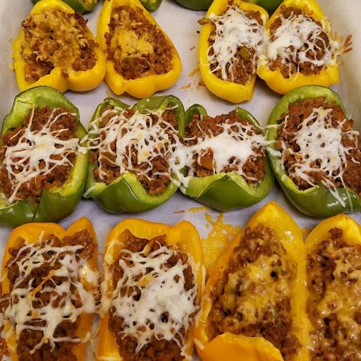 Green and yellow bell peppers with cooked ground beef topped with shredded cheese on a baking sheet.