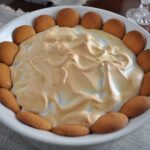 Southern Banana Pudding with Nilla Wafers and Meringue Topping in a White Casserole Dish on a tablecloth with crystal candle holder.