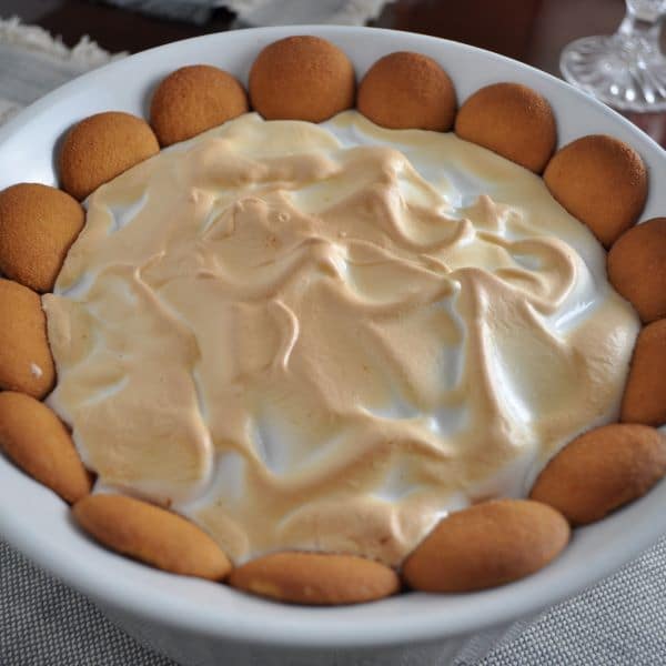 Southern Banana Pudding with Nilla Wafers and Meringue Topping in a White Casserole Dish on a tablecloth with crystal candle holder.