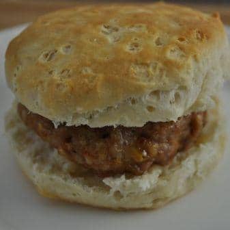 Sausage cooked in oven for a sausage breakfast sandwich made with biscuit sitting on a white plate.