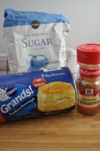 Can of grands biscuits, container of ground cinnamon and bag of sugar.