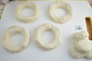 Prepared biscuit dough cut in for rings for air fryer donuts with remaining dough centers stacked on side.