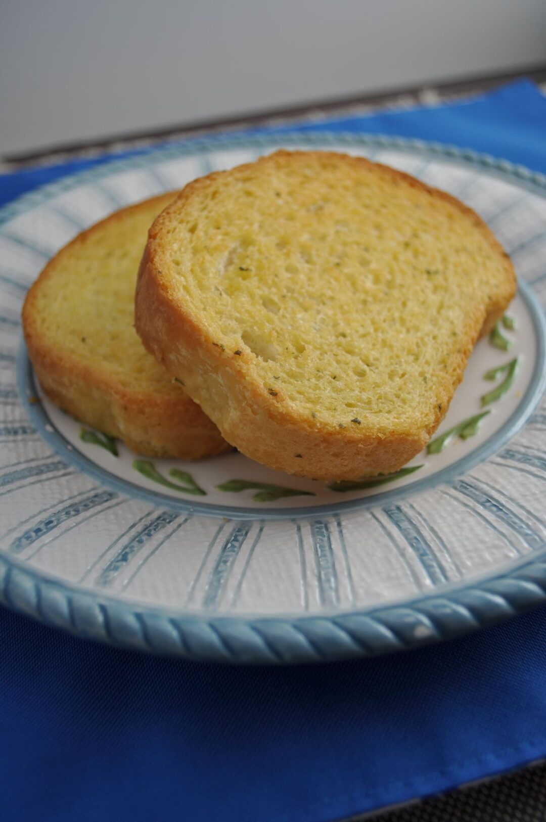 Two pieces of golden colored garlic Texas Toast on a blue and white plate sitting on a blue placemat.