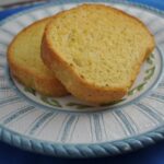 Two pieces of golden colored garlic Texas Toast on a blue and white plate sitting on a blue placemat.