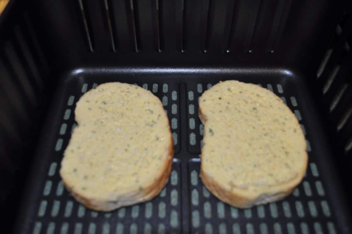Two pieces of frozen Texas toast in air fryer basket ready to cook.