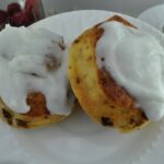 Two air fried cinnamon rolls with cream cheese icing on a plate.