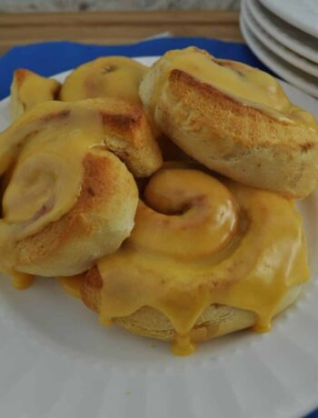 Orange cinnamon rolls baked in an air fryer on a plate dripping with sweet orange icing.