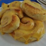 Orange cinnamon rolls baked in an air fryer on a plate dripping with sweet orange icing.