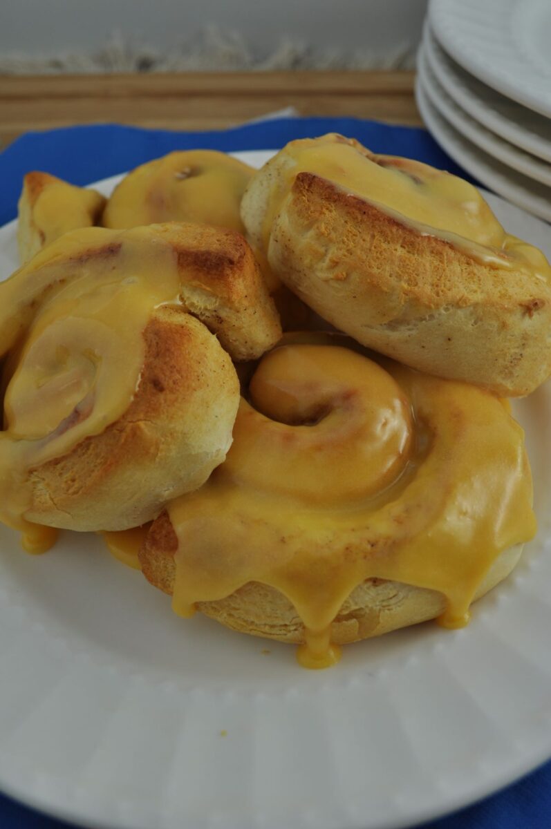 Orange cinnamon rolls baked in an air fryer on a plate dripping with sweet orange icing.