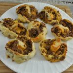 Cheesy sausage pinwheels baked and served hot on a serving plate.