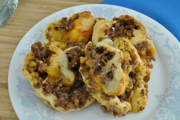 Four baked breakfast sausage crescent pinwheels rolled up and ready to eat served on a serving plate.