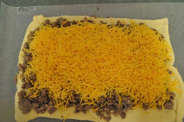 Crescent roll dough with cooked ground sausage and shredded cheddar cheese on top.