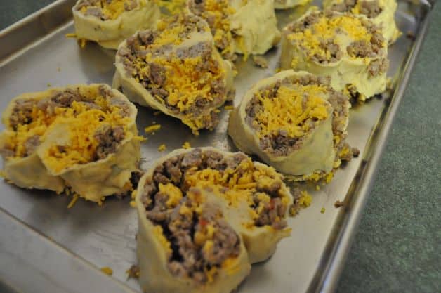 Sausage and cheese roll up in crescent roll dough on a cookie sheet ready to bake.