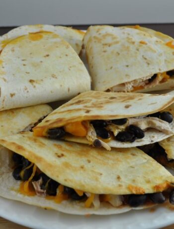 Blackstone quesadillas prepared on the griddle and arranged on a white plate. The quesadillas are cut into quarter pieces and are filled with chicken, black beans, salsa and cheese.
