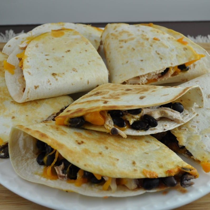 Blackstone quesadillas prepared on the griddle and arranged on a white plate. The quesadillas are cut into quarter pieces and are filled with chicken, black beans, salsa and cheese.