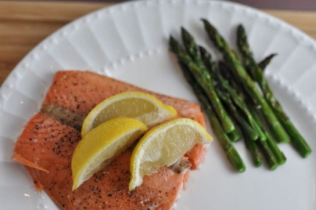 Baked salmon at 350 with 3 lemon wedges on a plate with asparagus spears.