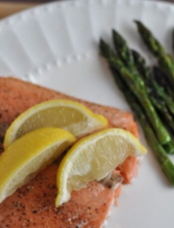 Baked salmon at 350 with 3 lemon wedges on a plate with asparagus spears.