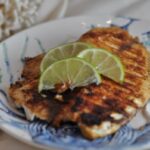 Grill tilapia will lime slices on a plate.