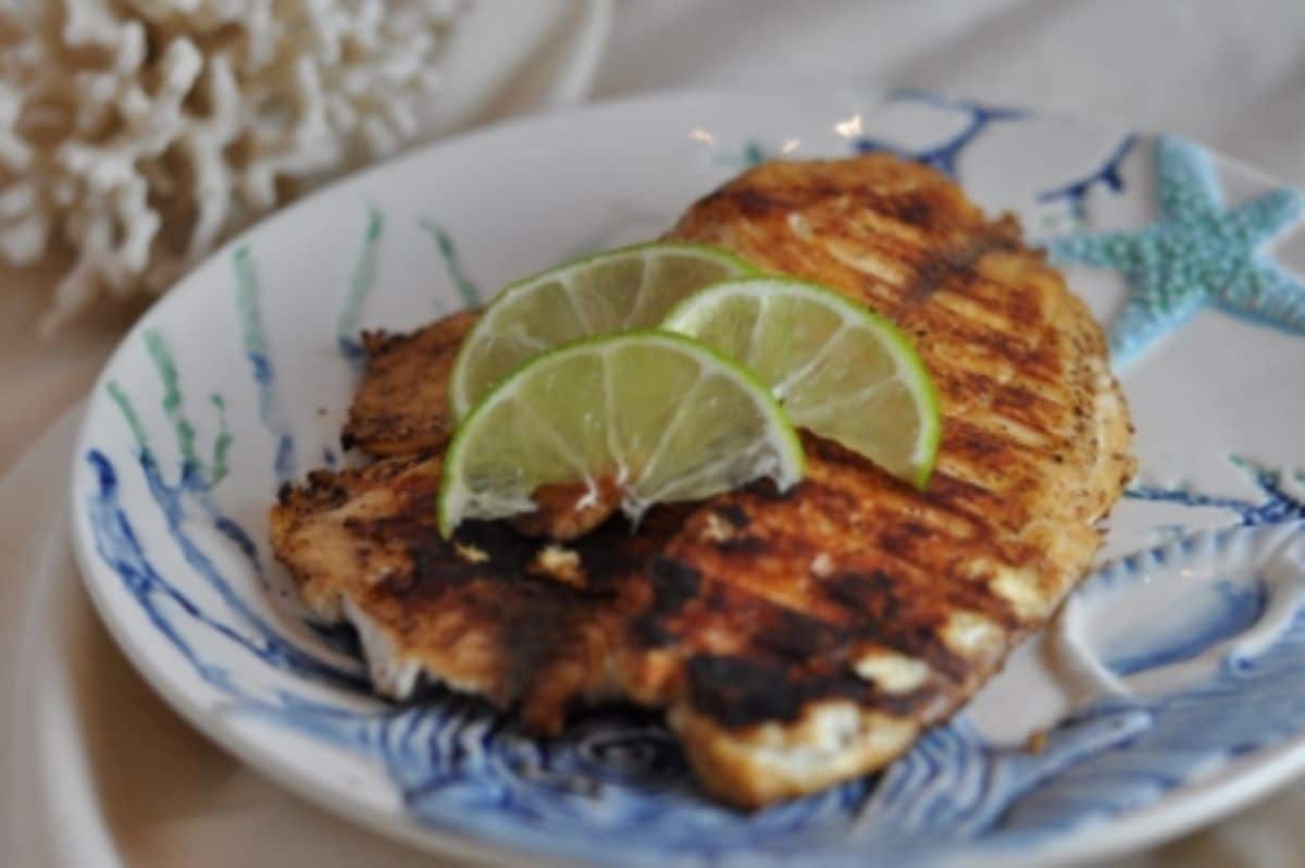 Grill tilapia will lime slices on a plate.