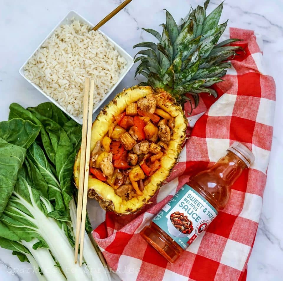 Blackstone Sweet Tangy Pineapple Chicken in a half pineapple on a red checked tablecloth.