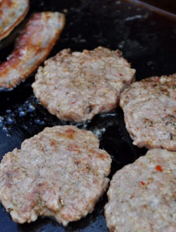 Sausage patties cooking on a Blackstone griddle with bacon.