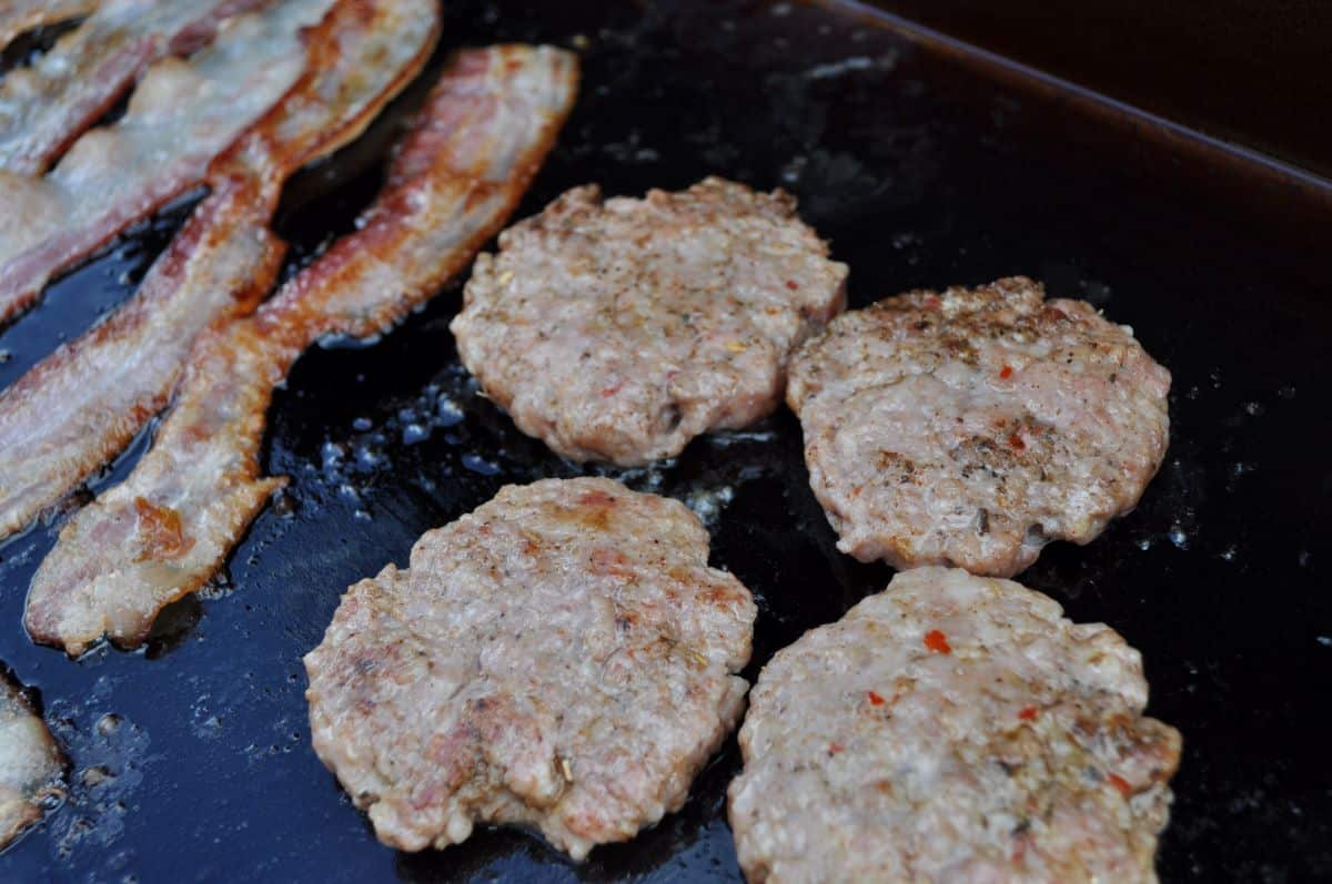 Sausage patties cooking on a Blackstone griddle with bacon.
