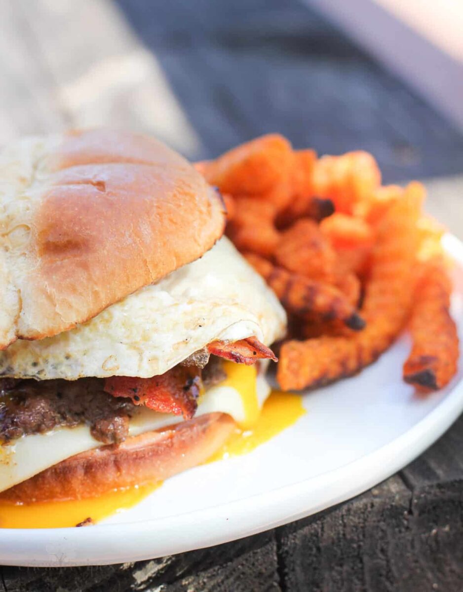 Hamburger grilled on blackstone griddle with french fries on a white plate.