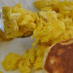 Scrambled eggs prepared on blackstone griddle on a plate with biscuits.