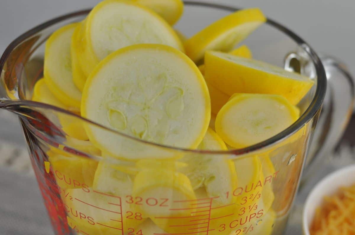 Easy squash casserole recipe made with sliced yellow squash in a glass measuring cup.