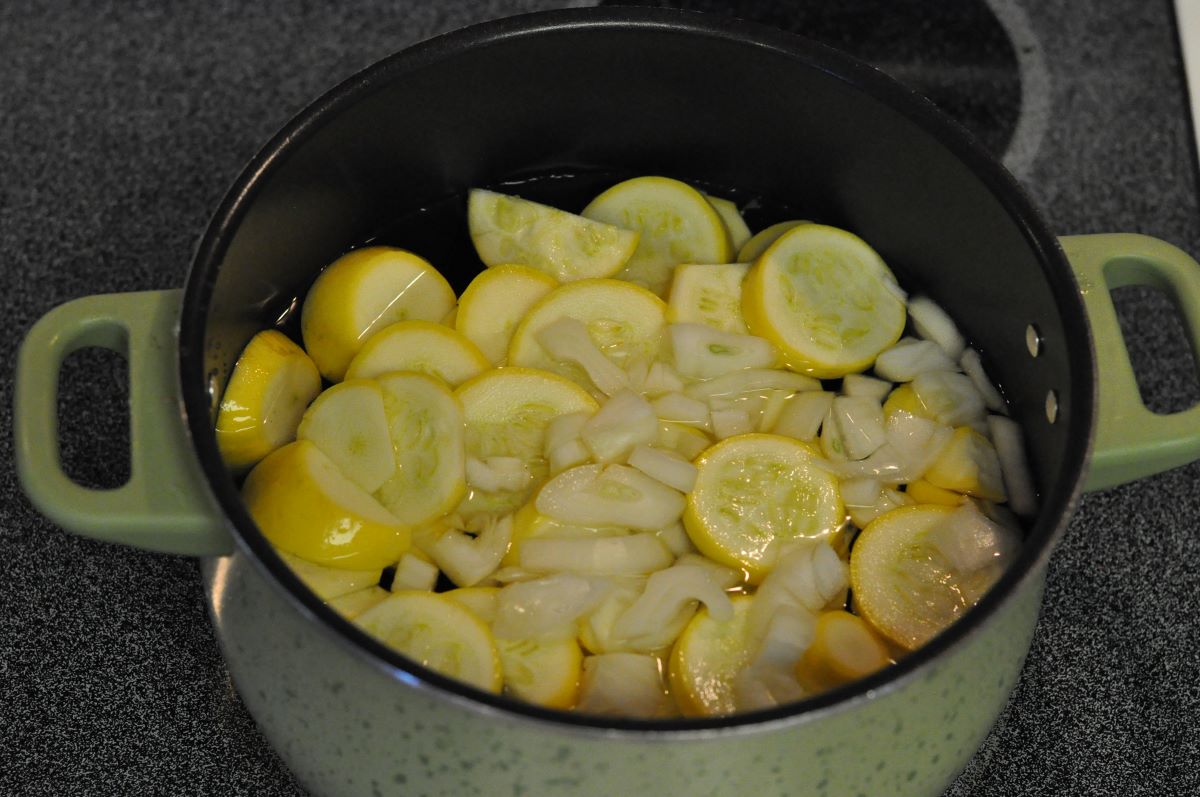 Easy squash casserole recipe ingredients of yellow squash slices and chopped onions in a boiler ready to cook for a casserole.