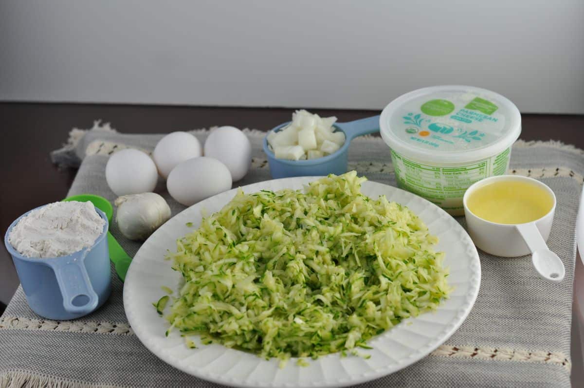 Zucchini souffle ingredients including shredded zucchini, bisquick, garlic, eggs, butter, onions and parmesan cheese.