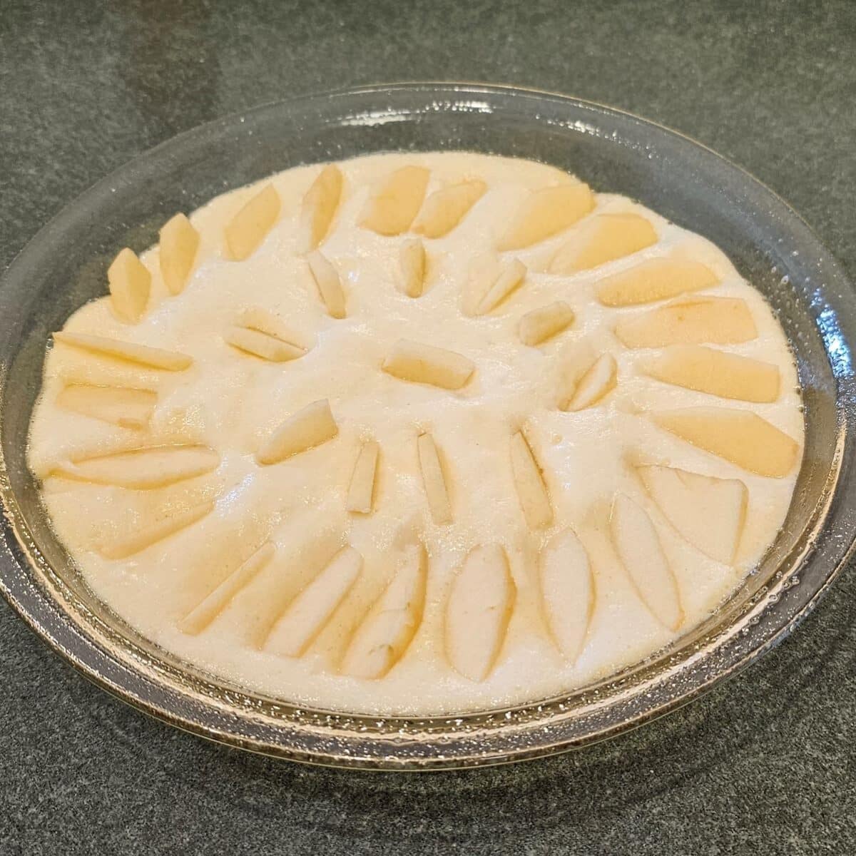 German Pancakes Recipe step before baking in an oven for arranging apples on top of German Pancake batter in a circular pattern.