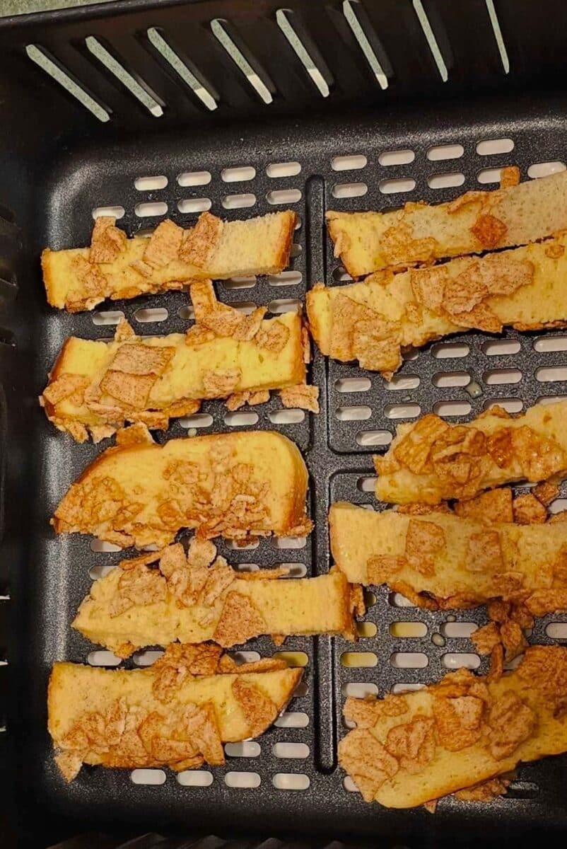French toast sticks rolled in eggs, milk and cinnamon crunch cereal ready to cook in the air fryer basket.